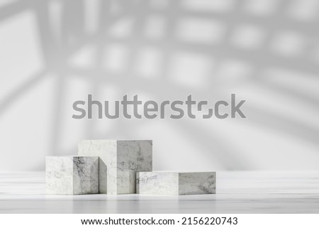 Simple podium as showcase for products. Modern showcase with three marble cube podium with palm leaf in sunlight, shadow on white board, grey wall, cosmetic goods Royalty-Free Stock Photo #2156220743