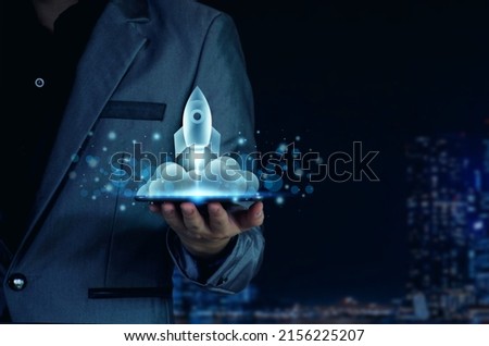 Startup business concept. Businessman holding a tablet, rocket launching and soar flying out from screen, starting a business, growing business, modern technology, hologram, network connection. Royalty-Free Stock Photo #2156225207