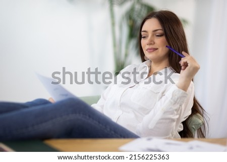A girl in a shirt sits near the table and draws ideas on paper and in a notebook in the room