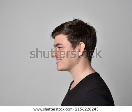 close up portrait of young brunette man, head and shoulders wearing basic black shirt, with expressive dramatic facial expressions, isolated on studio background.