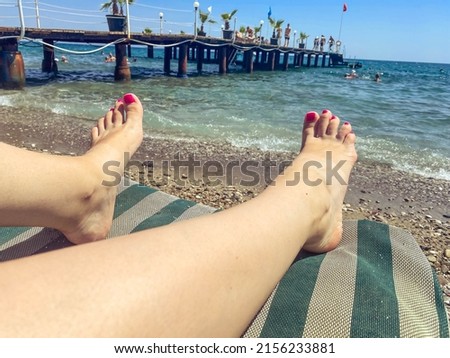 a girl with a bright gel polish on her legs stands on a sunbed. tan under the bright sun. woman with pedicure resting on the sea next to the water.