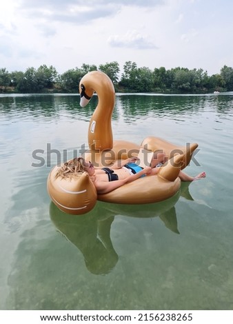 young woman on holiday. girl relaxing on water. lady reading a book and lying on big golden inflatable shaped as swan. lake or sea. happiness and joy. sunbathing.
