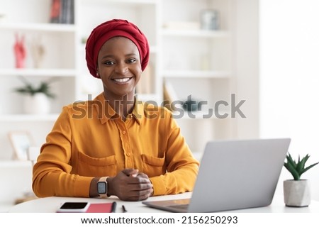 Stylish muslim african american woman in casual outfit sitting at worktable, working on laptop, smiling at camera, posing alone at cozy office, copy space. Millennials business concept Royalty-Free Stock Photo #2156250293