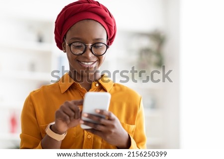 Closeup portrait of positive stylish young black lady in red turban using modern smartphone, SMM-manager chatting with clients or posting content, working online, panorama with copy space Royalty-Free Stock Photo #2156250399