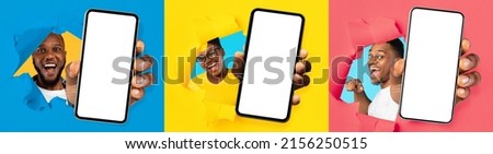 Glad excited millennial african american guys and woman with open mouths look through hole in colorful paper and show smartphones with empty screen. App and ad, huge sale, great offer and victory Royalty-Free Stock Photo #2156250515