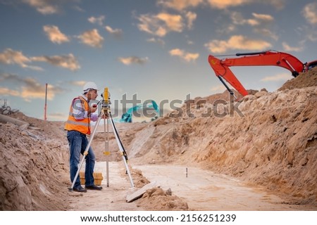 Surveyor engineers wearing safety uniform ,helmet and radio communication with equipment theodolite to measurement positioning on the construction site of the road with construct machinery background. Royalty-Free Stock Photo #2156251239