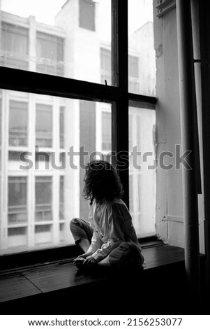 Girl sits and looks through the window. Black and white photo. Loneliness. Feeling sad Royalty-Free Stock Photo #2156253077