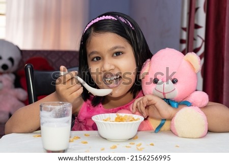 An Indian girl child eating cereal with milk with smiling face and looking at camera