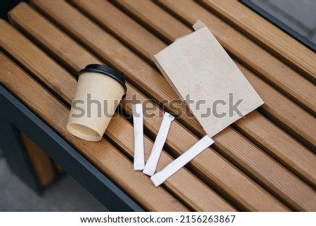 Paper cup and sticks with sugar. Paper cup with coffee with lid. Summer day, rays and flashes of the sun. Warm color tone. Coffee in a paper cup.