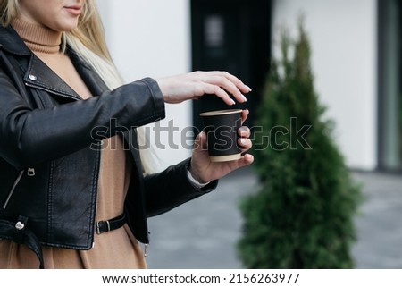 The girl closes a paper cup. Paper cup in the hands of a girl. Girl holding coffee in a paper cup.