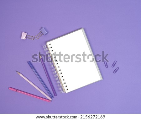 Open blank sketchbook, liners and pencils on purple background. Copy space, flat lay