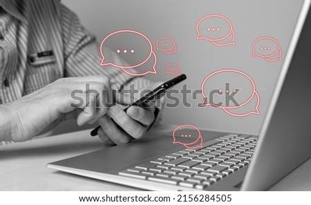 Man using phone for responding to negative feedback and reviews, bad comments, customers claims and complaints. Male sitting at table with laptop. Black and white. High quality photo Royalty-Free Stock Photo #2156284505