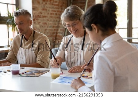 Three older and young art-school students painting with acrylic paints on paper looks inspired, engaged in creative hobby in group class. Improve skills, gain professional artistic education concept Royalty-Free Stock Photo #2156291053