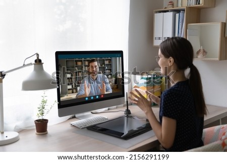 Focused engaged intern, student talking to coach, teacher, making video call, using desktop computer with big monitor. Freelance employee, designer discussing project with client, customer Royalty-Free Stock Photo #2156291199