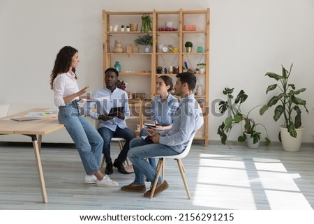 Diverse millennial business team meeting in modern office eco interior, sitting in circle, talking, holding documents, gadgets. Boss discussing project with employees. Mentor training interns Royalty-Free Stock Photo #2156291215