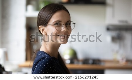 Happy young millennial woman wearing glasses posing in home kitchen banner head shot portrait. Positive nerdy smart student girl in stylish eyewear looking at camera, smiling