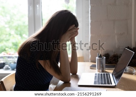 Exhausted upset young student girl sitting at table with laptop, leaning head on hand, suffering from headache, feeling depressed, unhappy, tired, getting bad news. Professional burnout concept Royalty-Free Stock Photo #2156291269