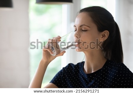 Thirsty dehydrated young woman drinking cold clean water from glass at home, swallowing beverage with closed eyes, recovering hydration balance, keeping healthy habit, lifestyle