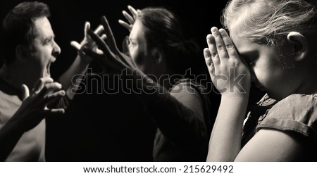 Child prays for peace in the family on the background of quarreling parents. MANY OTHER PHOTOS FROM THIS SERIES IN MY PORTFOLIO.  Royalty-Free Stock Photo #215629492