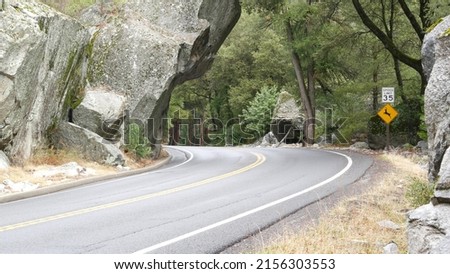 Yellow warning sign deer crossing, curve in woods, forest trees. Trip or roadtrip to Yosemite, Tioga road, California wildlife fauna, animals in USA. Ecotourism in wild nature or hitchhiking traveling Royalty-Free Stock Photo #2156303553