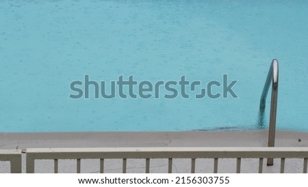 Rain drops falling on water surface of blue swimming pool, rainy day in motel or hotel, California USA. Rainfall on summer vacations, raindrops splashing during monsoon. Seamless looped cinemagraph. Royalty-Free Stock Photo #2156303755
