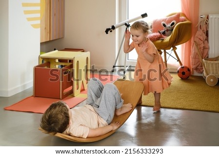 Child playing on balance Board for Toddlers in kids room. Curvy Rocker Board used for motor physical development at home. Girl and boy playing, get fit, stretch back in yoga exercises Royalty-Free Stock Photo #2156333293