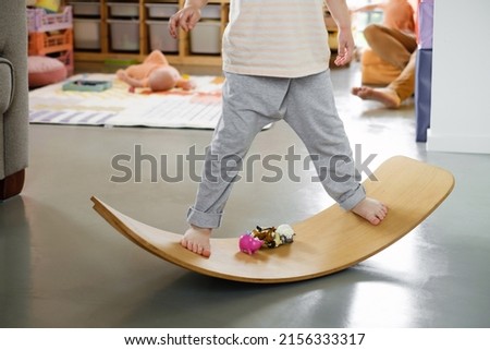 Child playing on balance Board for Toddlers in kids room. Curvy Rocker Board used for motor physical development at home. Boy playing, get fit with toys. Legs closeup Royalty-Free Stock Photo #2156333317