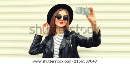 Portrait of beautiful happy woman taking selfie with smartphone posing wearing black round hat on white background