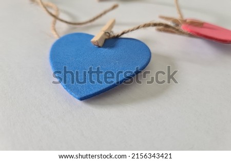HEART OF VARIOUS COLORS ON A WHITE BACKGROUND HANGING FROM TWEEZERS