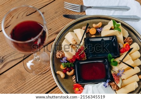 There is a dish on the wood table with utensils and a glass. We can see a red sauce, an oil, macaroni, some fruits, such as cherry. The small flower is decoration the tasty dish. It looks amazing.