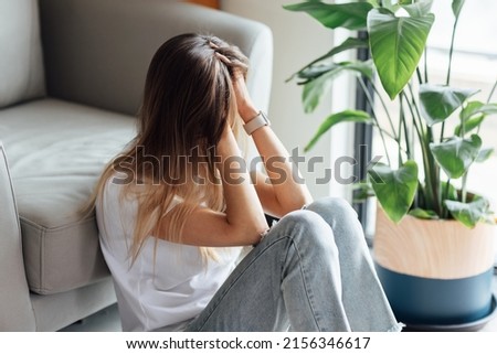 Unhappy young caucasian woman with blonde hair thinking about bad relationships problems, break up with boyfriend. Worried millennial girl sitting on floor in bedroom near chair and green plant alone Royalty-Free Stock Photo #2156346617