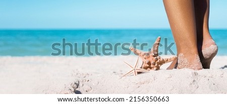 Starfishes lie next to female feet on a sandy beach. Banner.