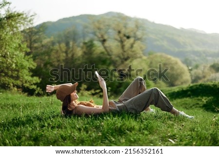 Happy woman blogger lying on the grass in the park and smiling with her phone in her hands against the backdrop of a summer natural landscape with sunlight Royalty-Free Stock Photo #2156352161