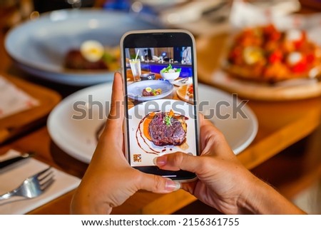 Technology and social network in people life. Woman holds phone and makes photos for social media before eating luxury fine food. Food photography or blogger