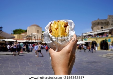Pita Gyros. Greek gyros wrapped in pita breads against Greek old city square. Royalty-Free Stock Photo #2156362857