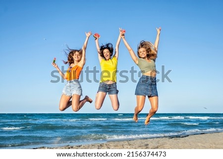 three happy girls on jumping motion at the sand beach outdoors in summer celebrating hot vacation days. happy funny friends having fun on warm seaside holidays joy, carefree, genz and party concept Royalty-Free Stock Photo #2156374473