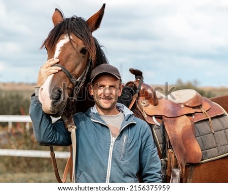 Portrait of a young man rider with brown horse next to wooden fencing