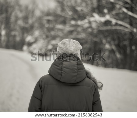 Girl in a hat and jacket on a background of snowy winter. Rear view. Winter season. Black and white photo. 