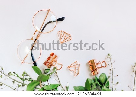 Glasses, paper clips and clips in the form of rose gold diamonds on a background with green plants.