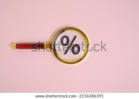 Percentage sign under magnifying glass, on pink background