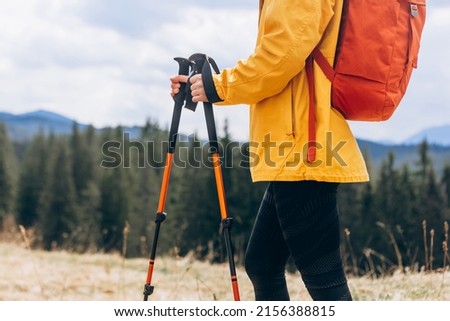 Close up Hiker with trekking poles goes against mountain landscape. Hiking and travel concept Royalty-Free Stock Photo #2156388815
