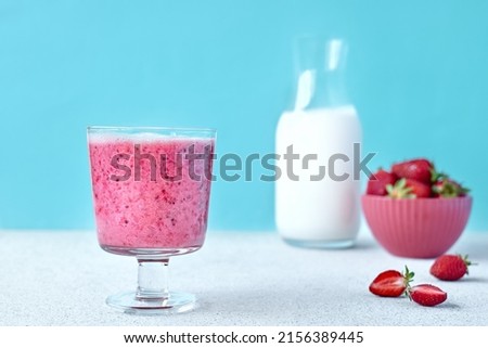 Strawberry coconut milkshake, frappé or smoothie in drinking glass on light blue background. Healthy vegan diet refreshing drink. Healthy food and drink concept. Selective focus.