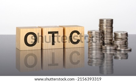 otc - text is made up of letters on wooden cubes lying on a mirror surface, gray background. stacks with coins. inscription is reflected from the surface. otc - short for Over The Counter Royalty-Free Stock Photo #2156393319