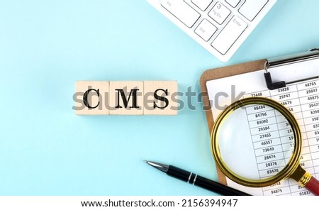 CMS word on wooden cubes on a blue background with chart and keyboard