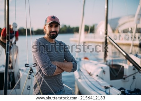 Preparation for the regatta at the yachting school at the marina with sailing yachts. A young male yachtsman prepares a moored sport yacht for sailing at sunset. Royalty-Free Stock Photo #2156412133