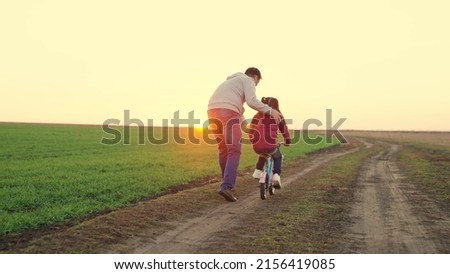 Father teaches little kid girl to ride child's bike on road, in fall, in spring. Happy family, dad teaches his daughter, child to ride bike in park at sunset. Happy family, childhood. Parent, child Royalty-Free Stock Photo #2156419085