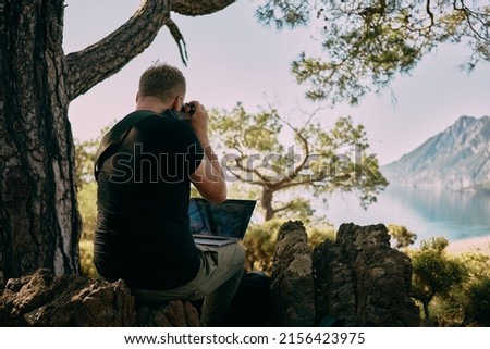Man sitting on the top of mountain and taking photo straight to laptop. Remote worker. High quality photo