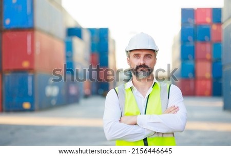 Man manager cross arm. Handsome caucasian male dock foreman worker in white hard hat helmet and high-visibility vest walking in Shipping Cargo Container Terminal Depot