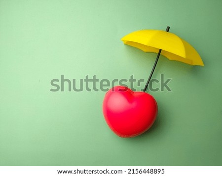 Red heart with yellow umbrella on a green background.