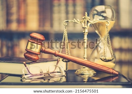 Legal office of lawyers, justice and law concept : Judge gavel or a hammer and a base used by a judge person on a desk in a courtroom with blurred weight scale of justice, bookshelf, hourglass behind. Royalty-Free Stock Photo #2156475501